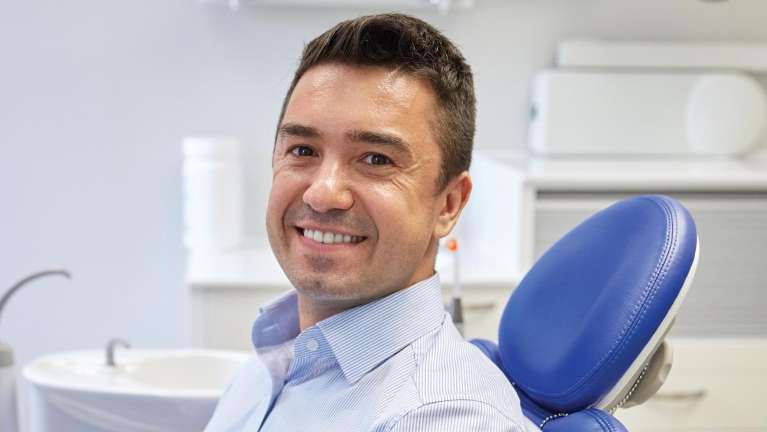 man sitting in dentist chair smiling | veneers boulder